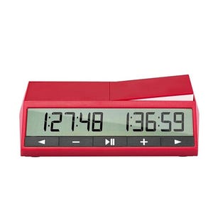 May include: A red digital chess clock with a green display showing two time displays. The clock has black control buttons and a flip-up top. The time displays show 1:27:48 and 1:36:59.