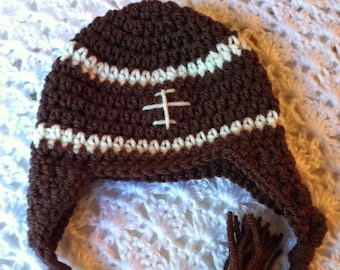 May include: Brown crocheted hat shaped like a football with a white stitched design. The hat has a long brown tassel.