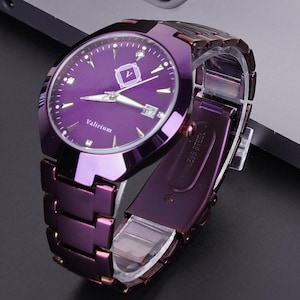 May include: A purple wristwatch with a matching strap is displayed on a dark surface, next to a laptop and a smartphone. The watch face shows the date and the brand name "Valiziom". The watch has a metallic finish.