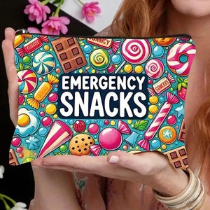 May include: A rectangular cosmetic bag with a black zip, decorated with a vibrant candy design. The bag showcases illustrations of sweets like lollipops and chocolates, with the text "EMERGENCY SNACKS" in white. The background is a mix of blue and yellow.