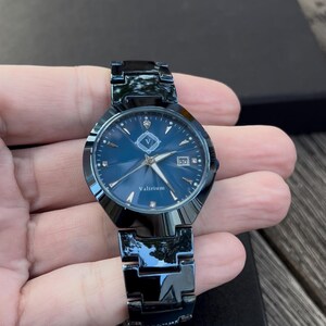 May include: A dark blue watch with a matching metal band. The watch face is also dark blue with silver hands and markers. The watch has the word "Valirium" printed on the face and a date display at the 3 o'clock position.
