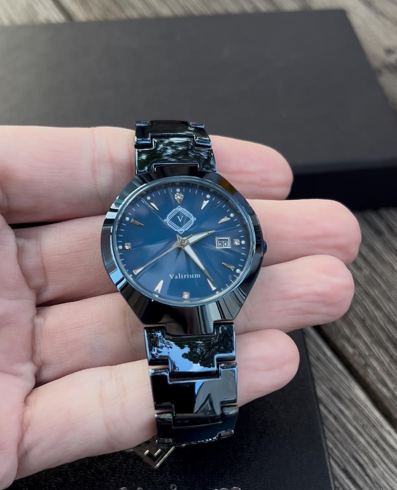 May include: A dark blue watch with a matching metal band. The watch face is also dark blue with silver hands and markers. The watch has the word "Valirium" printed on the face and a date display at the 3 o'clock position.