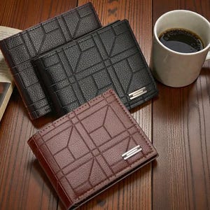 May include: Three leather wallets in black and brown, featuring a geometric design and a silver accent. A white mug of coffee sits nearby on a wooden surface. The wallets are closed and appear unused.