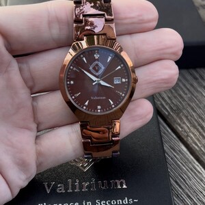 May include: A rose gold wristwatch with a brown face and matching band. The watch face features a date display and small diamond-like markers. The brand name "Valirium" is visible on the watch face and the watch box.