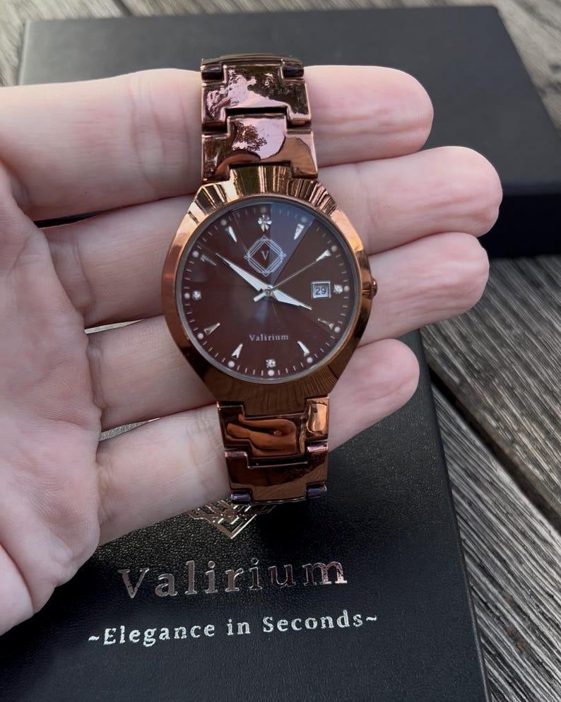 May include: A rose gold wristwatch with a brown face and matching band. The watch face features a date display and small diamond-like markers. The brand name "Valirium" is visible on the watch face and the watch box.
