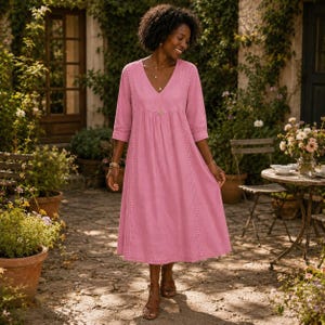 May include: A midi-length pink dress with three-quarter sleeves, a V-neckline, and vertical lace trim detailing along the front bodice. The garment features a gathered waistline and a loose, flowing skirt that falls below the knees.
