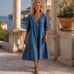 May include: A midi-length blue denim dress featuring a V-neckline, three-quarter length sleeves, and vertical lace-like trim detailing along the front. The dress has a loose, flowing silhouette and is paired with brown strappy sandals.