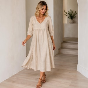 May include: A beige midi-length dress with a V-neckline, three-quarter length sleeves, and vertical lace trim detailing along the bodice. The garment features a loose, flowing silhouette with a gathered waistline and a simple, solid-colored fabric.