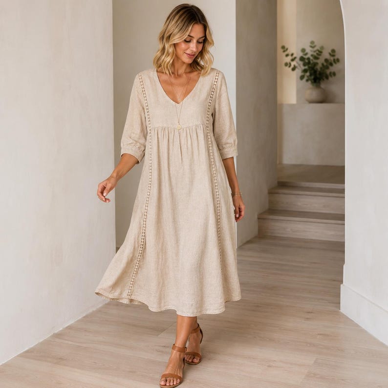 May include: A beige midi-length dress with a V-neckline, three-quarter length sleeves, and vertical lace trim detailing along the bodice. The garment features a loose, flowing silhouette with a gathered waistline and a simple, solid-colored fabric.