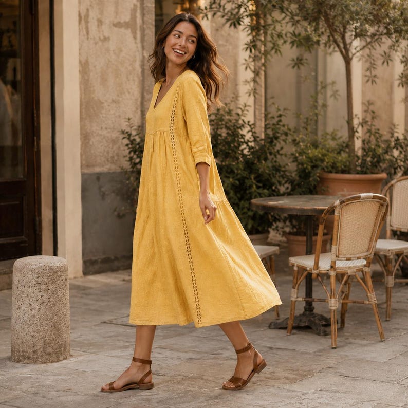 May include: A long, mustard yellow dress with three-quarter length sleeves, a V-neckline, and vertical lace-like trim detailing running down the front. The dress features a loose, flowing skirt and is paired with simple brown strappy sandals.