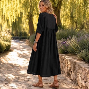 May include: A black midi-length dress featuring three-quarter length sleeves, a round neckline, and vertical lace trim detailing along the sides. The garment has a loose, flowing silhouette that falls below the knees, paired with brown sandals.