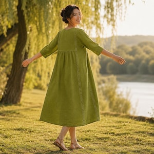 May include: A midi-length olive green dress featuring three-quarter length sleeves, a round neckline, and vertical lace trim detailing running down the front panels. The garment has a loose, flowing silhouette with a gathered waistline seam.