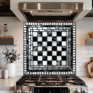 May include: A kitchen backsplash with a checkerboard pattern in black and white. The backsplash is made of small, irregular tiles and is framed by a border of smaller, lighter-colored tiles. The backsplash is above a stainless steel gas range.