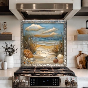 May include: A decorative kitchen backsplash featuring a beach scene with a blue sky, clouds, and ocean. The artwork includes sand, seashells, and tall grass, framed in a silver metal border. The backsplash is installed above a stainless steel gas stove.