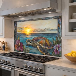 May include: A kitchen with a stainless steel stove and a decorative backsplash featuring a stained glass design of a sea turtle, sunset, and flowers. The kitchen has white cabinets, a woven pendant light, and a view of the ocean.