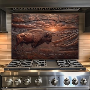 May include: A bronze-colored, relief-style artwork depicting a bison in a grassy field under a sunset sky. The artwork is mounted above a stainless steel stove, adding a rustic touch to the kitchen decor.