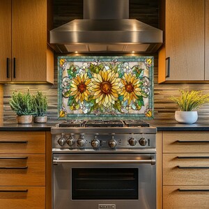 May include: A stained glass panel featuring three large sunflowers with yellow petals and brown centers. The panel is framed with a teal border and is installed above a stainless steel stove in a kitchen setting.