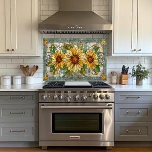 May include: A kitchen backsplash featuring a stained glass design with three large sunflowers in shades of yellow, orange, and brown. The sunflowers are surrounded by green leaves and a teal border. The backsplash is installed above a stainless steel range.