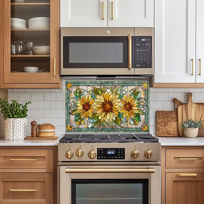 May include: A decorative kitchen backsplash featuring a stained glass design with three large sunflowers. The sunflowers have yellow petals and brown centers, surrounded by green leaves and white flowers. The backsplash is framed with a green border.