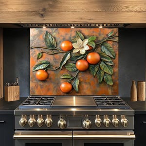 May include: A decorative metal wall art piece featuring a branch with oranges, green leaves, and a white flower. The artwork has a textured, orange and brown background. The art is mounted above a stainless steel gas range.