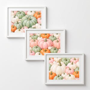 May include: Three white-framed wall art prints featuring watercolor-style illustrations of pumpkins in various shades of sage green, soft pink, bright orange, and creamy white, arranged in a dense, overlapping composition across each rectangular frame.