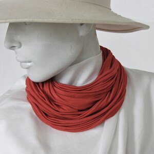 Könnte beinhalten: Ein weißer Hut mit breiter Krempe und ein roter Stoffschal, der um den Hals getragen wird. Der Schal besteht aus einem weichen, dehnbaren Material und hat ein plissiertes Design.