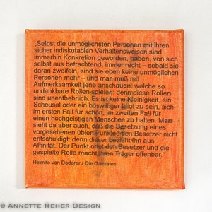 Könnte beinhalten: Orangefarbene Leinwandkunst mit schwarzem Text. Der Text ist ein Zitat aus Heimito von Doderers "Die Dämonen". Das Kunstwerk hat ein strukturiertes Aussehen und ist unten mit "ANNETTE REHER DESIGN" signiert.