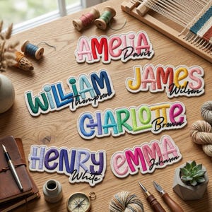 May include: Embroidered name patches in various colors, including red, blue, and yellow, with names like Amelia, James, and Charlotte. The patches are displayed on a wooden surface with crafting supplies such as spools of thread and yarn.