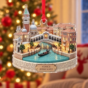 May include: A flat, multi-layered acrylic Christmas ornament depicting a Venetian canal scene with the Rialto Bridge, St. Mark's Campanile, and a gondola. The base features a plaque with the text VENICE JESSICA2025 and a red ribbon for hanging.