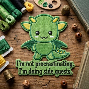 May include: Embroidered green dragon patch with yellow accents and the text "I'm not procrastinating. I'm doing side quests." The patch is surrounded by spools of thread, a wooden palette with paint, thimbles, and beads on a wooden surface.
