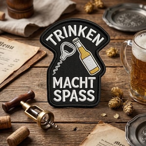 May include: A black patch with white embroidered text and a beer bottle and bottle opener design. The text reads "TRINKEN MACHT SPASS". The patch is on a wooden surface with a beer mug and other beer-related items.