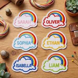 May include: Embroidered patches in the shape of a cloud and rainbow, each with a different name: Sarah, Oliver, Sophia, Ethan, Isabella, and Liam. The patches have a white background with colorful rainbow arcs and names in various colors.
