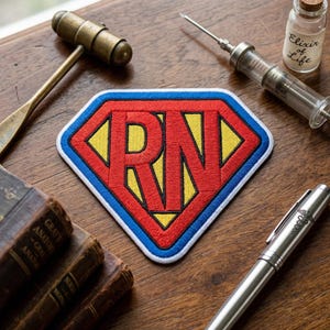 May include: A red, yellow, and blue embroidered patch with the letters "RN" in a diamond shape, reminiscent of a superhero logo. The patch is surrounded by medical tools, including a vintage syringe, a reflex hammer, and a small bottle labeled "Elixir of Life."