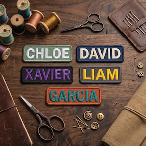 May include: A collection of personalized name patches in various colors, including green, blue, purple, gray, and orange. Each patch features a different name in bold, white or yellow lettering. Sewing supplies like scissors, spools of thread, and needles are arranged around the patches.