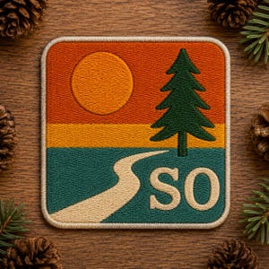 May include: A square embroidered patch featuring a landscape design with an orange sky, a yellow sun, a dark green pine tree, and a winding beige path leading toward the horizon. The letters SO are stitched in beige on the lower right side.