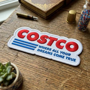 May include: Embroidered patch featuring the Costco logo in red, with blue stripes and the text "WHERE ALL YOUR DREAMS COME TRUE" on a white background. The patch is rectangular with a cloud-like border.