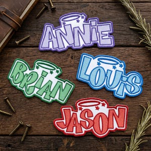 May include: Four embroidered name patches: "Annie" in purple, "Brian" in green, "Louis" in blue, and "Jason" in red. Each patch features a halo design with stars. The patches are on a wooden surface.