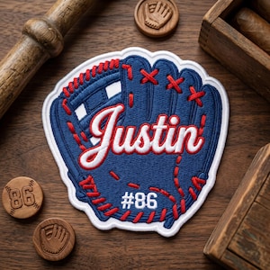 May include: A navy blue baseball glove patch with the name "Justin" in white script and the number "86". The patch has red stitching and a white border. Wooden baseball-themed accents surround the patch.