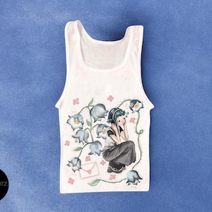 May include: White tank top with a floral and character design. The illustration features a girl listening to music surrounded by blue flowers and a letter. The tank top is on a blue background.