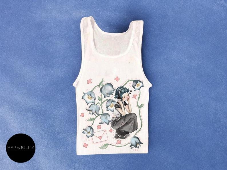 May include: White tank top with a floral and character design. The illustration features a girl listening to music surrounded by blue flowers and a letter. The tank top is on a blue background.