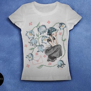 May include: White t-shirt featuring a watercolor illustration of a person wearing headphones, surrounded by blue flowers and musical notes. A pink envelope is also in the design. The shirt has a crew neck and short sleeves.