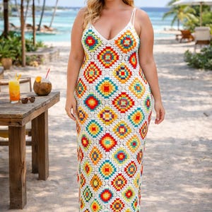 May include: A long, white crochet dress with a colorful geometric pattern of red, yellow, blue, and green squares. The dress has a V-neck and spaghetti straps. The model is wearing brown sandals on a sandy beach.