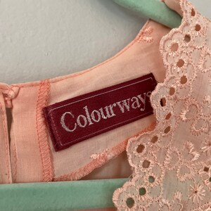 May include: A pale pink dress with a delicate lace trim around the neckline. The dress has a label that reads "Colourways".