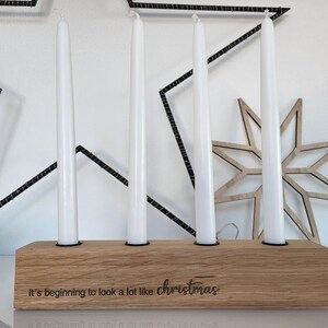 May include: A wooden candle holder with four white taper candles. The holder has the phrase "It's beginning to look a lot like christmas" engraved on it. A wooden star decoration is behind the candles.