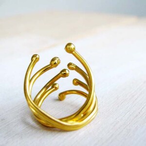 May include: A gold ring with a unique, abstract design featuring multiple curved lines and rounded ends.