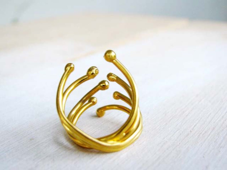May include: A gold ring with a unique, abstract design featuring multiple curved lines and rounded ends.