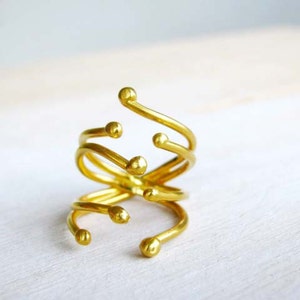 May include: A gold-toned ring with a unique, abstract design. The ring is made of multiple intertwined bands with rounded ends.