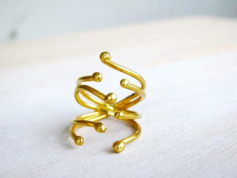 May include: A gold-toned ring with a unique, abstract design. The ring is made of multiple intertwined bands with rounded ends.