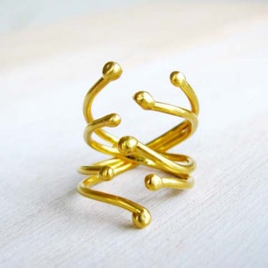 May include: A gold-toned ring with a unique, abstract design. The ring is made of multiple intertwined bands with rounded ends.