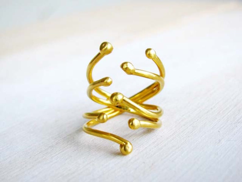 May include: A gold-toned ring with a unique, abstract design. The ring is made of multiple intertwined bands with rounded ends.